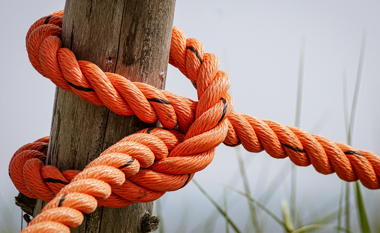 An orange rope is tied into a knot around a wooden post.